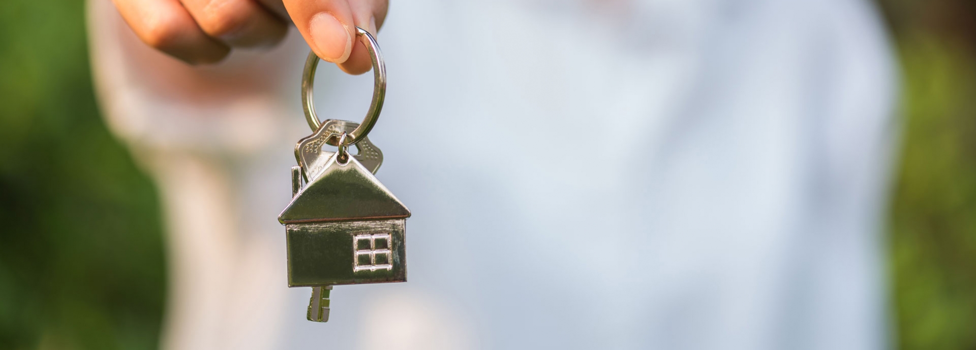 Een vrouw houdt de huissleutel vast met op de achtergrond groene bladeren