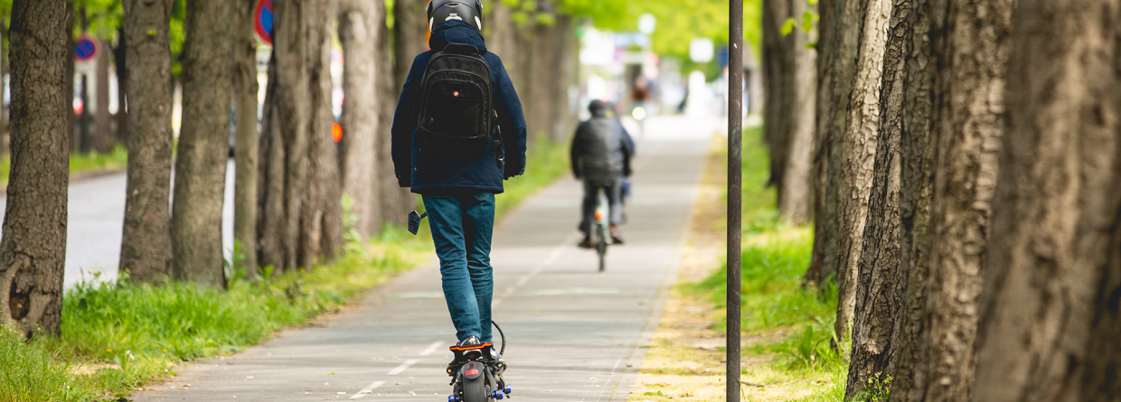 Een jongen op een elektrische step met een helm op en een rugtas