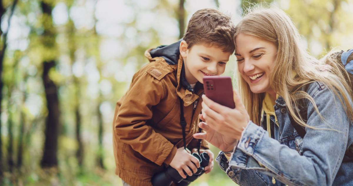 Gelukkige moeder en zoon wandelen in het bos. Ze gebruiken kaarten op smartphones.