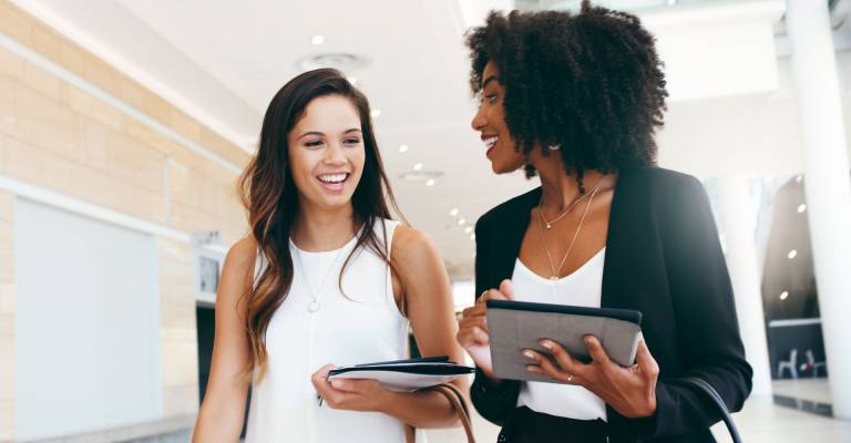 2 blijde jonge vrouwen lopen door het kantoor heen en hebben een overleg